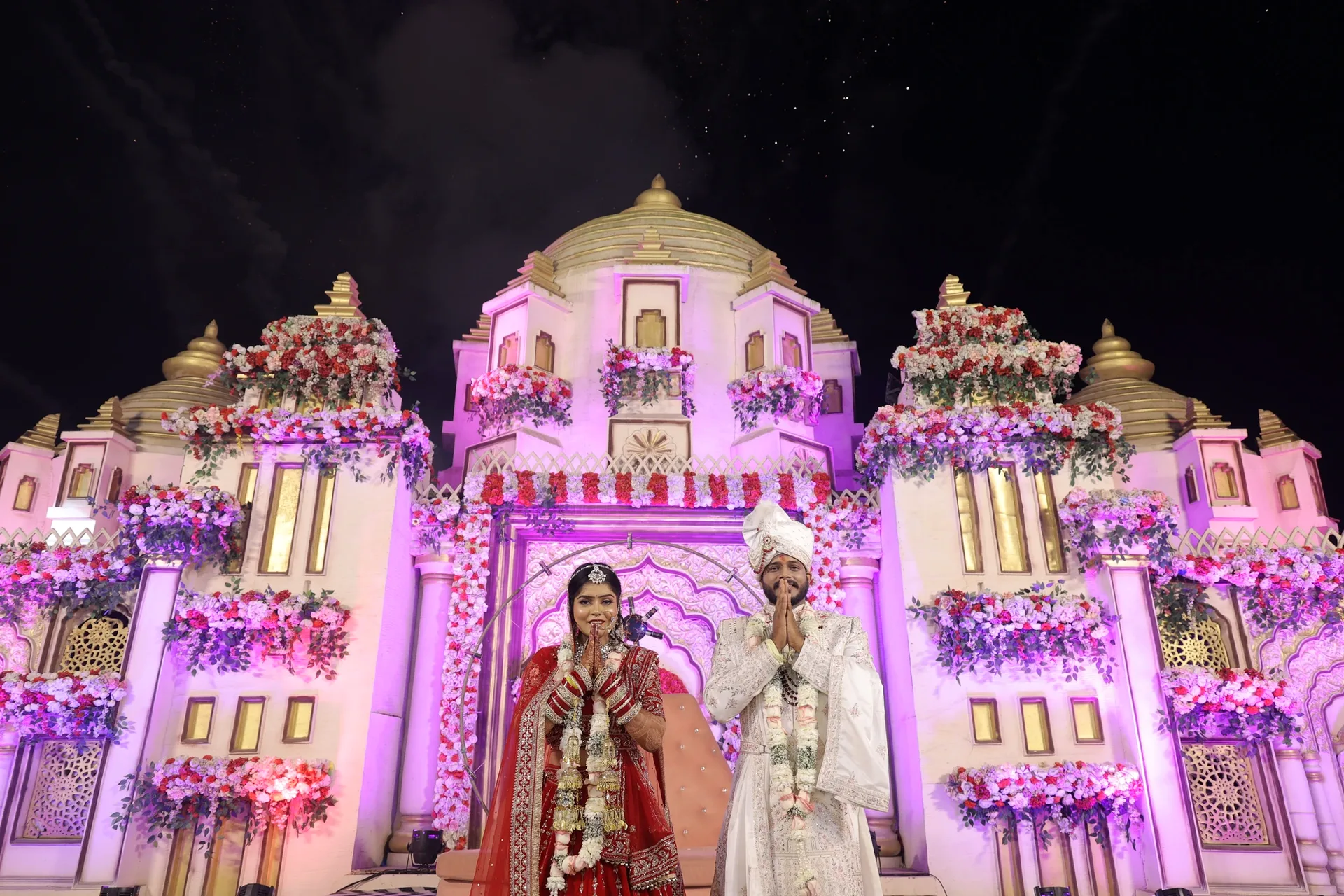 Varmala moment — palace decor wedding stage under the night sky